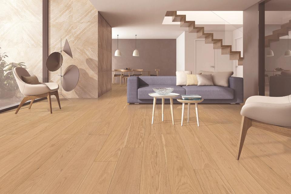 Warm toned hardwood flooring in living room with blue couch and grey chairs.